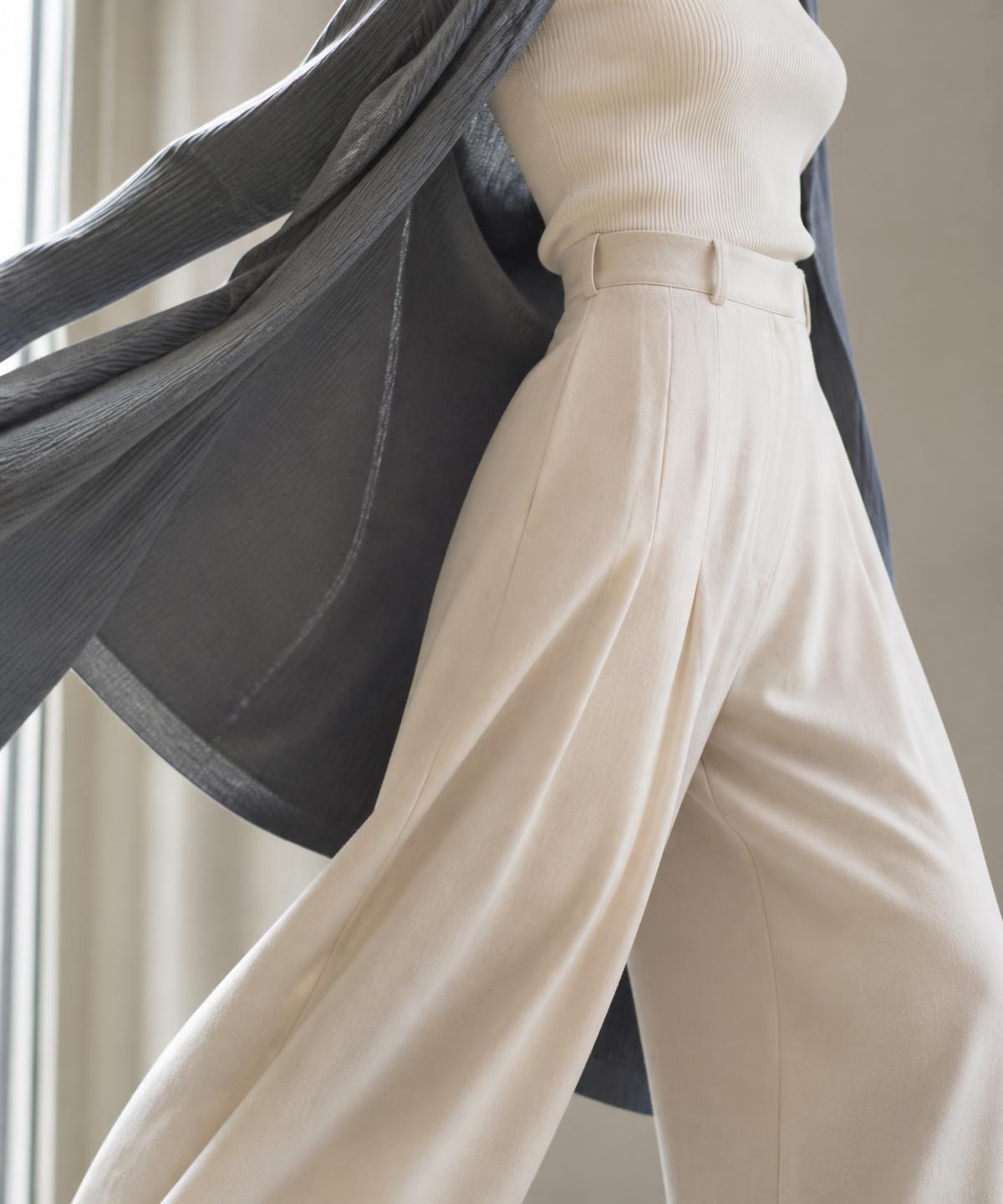 Close-up of Avaia cream wide-leg trousers and a fine knit top caught in movement